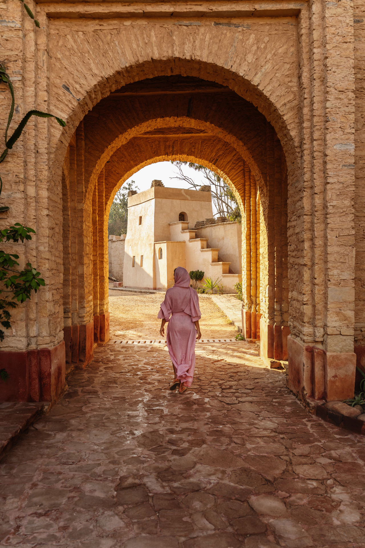 Woman in Pink Traditional Clothing Walking Through Historic Stone Archway in Marrakesh Medina.